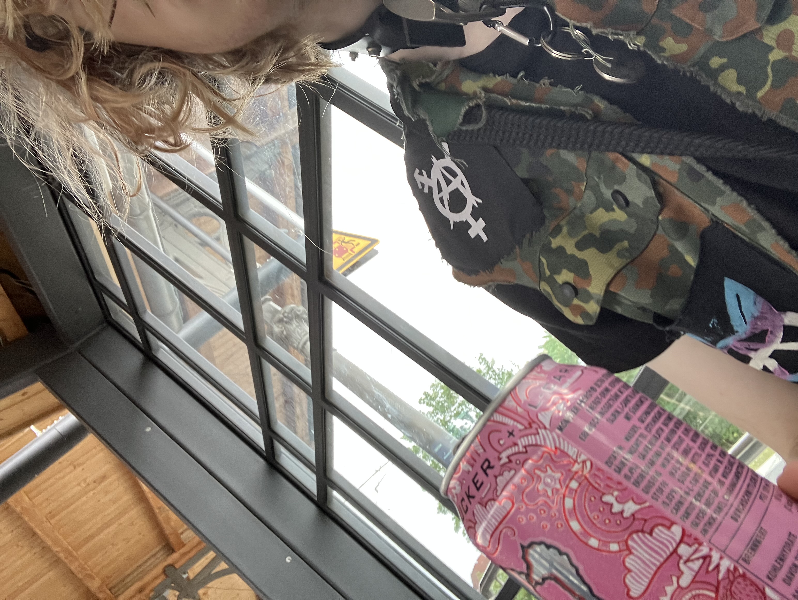 selfie without my face visible of me in a defaced camo vest with queer anarchist patches chillin at a train station